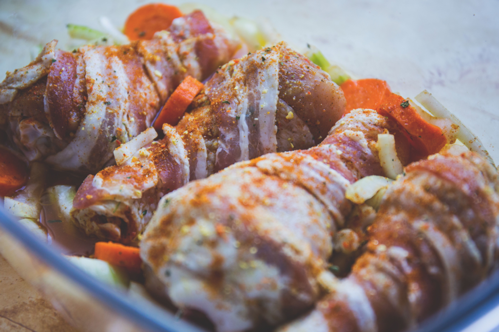 Chicken & Non-Vegetarian Recipes: Delicious bacon-wrapped chicken drumsticks seasoned with spices, ready for cooking with vegetables.